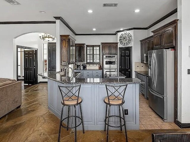 kitchen featuring dark brown cabinetry, appliances with stainless steel finishes, a peninsula, and arched walkways