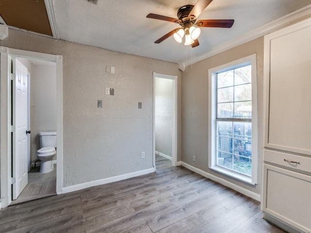 unfurnished bedroom featuring multiple windows, wood finished floors, baseboards, and a textured wall