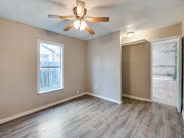 unfurnished bedroom with baseboards, wood finished floors, a textured ceiling, ensuite bath, and a ceiling fan