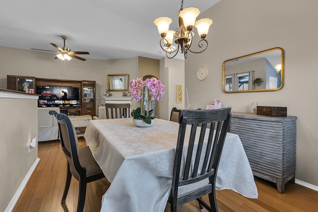 dining room featuring ceiling fan with notable chandelier, wood finished floors, and baseboards