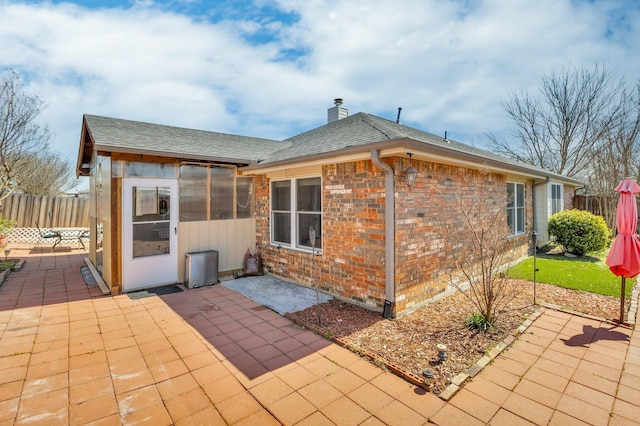 back of house featuring a patio, fence, roof with shingles, a chimney, and brick siding