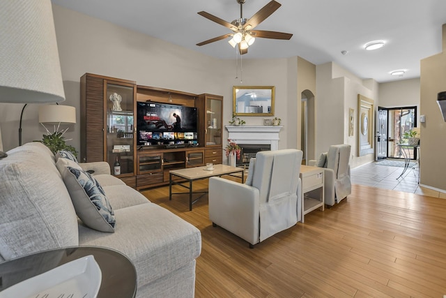 living room with a ceiling fan, wood finished floors, arched walkways, and a fireplace