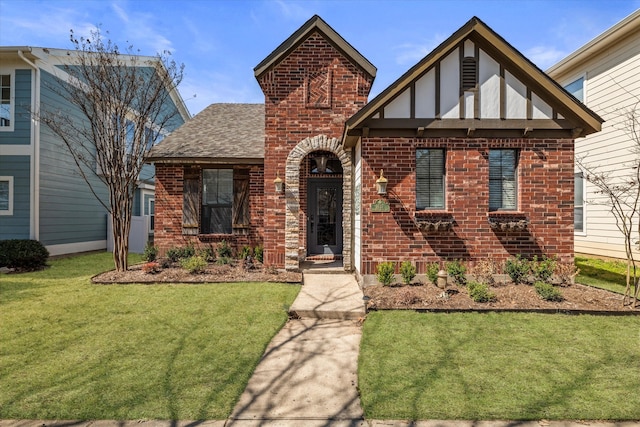 tudor-style house with brick siding, a front lawn, and roof with shingles