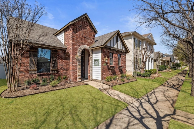 tudor-style house with a front yard, brick siding, and a shingled roof