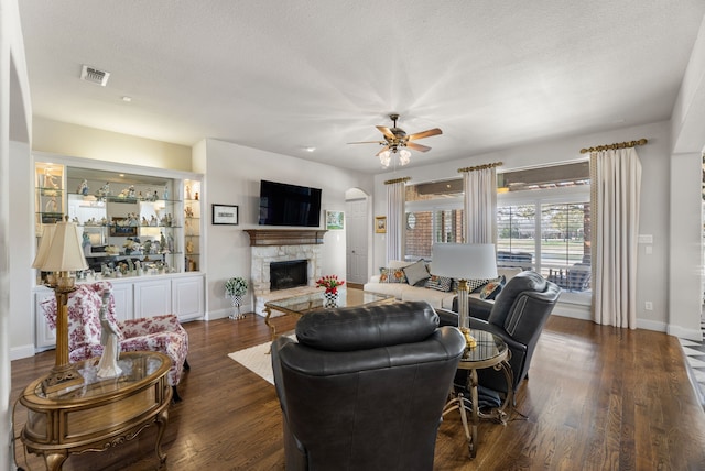 living room with a stone fireplace, baseboards, dark wood-style flooring, and ceiling fan