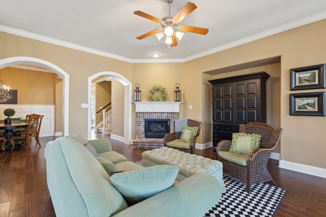 living room featuring a brick fireplace, baseboards, arched walkways, a ceiling fan, and dark wood-style flooring