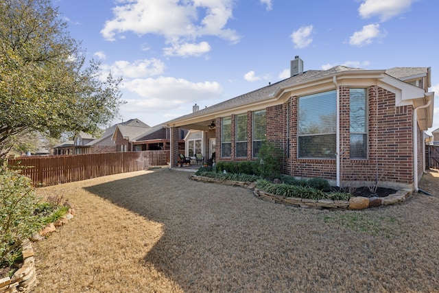 rear view of property featuring a patio, fence, brick siding, and a chimney