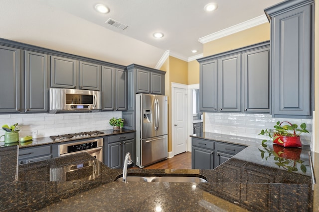 kitchen featuring visible vents, a sink, ornamental molding, stainless steel appliances, and backsplash