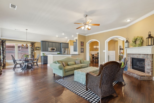 living room featuring visible vents, ceiling fan with notable chandelier, crown molding, a fireplace, and dark wood-style flooring