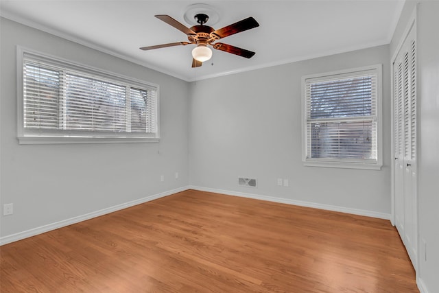 spare room with visible vents, a ceiling fan, light wood-style floors, crown molding, and baseboards