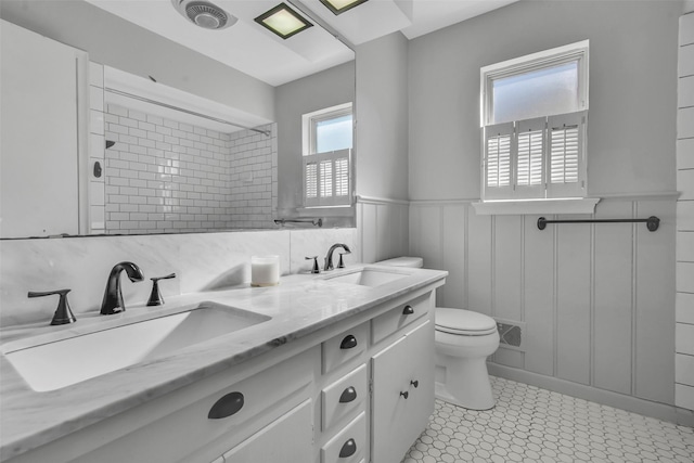 bathroom featuring a sink, visible vents, toilet, and a wainscoted wall