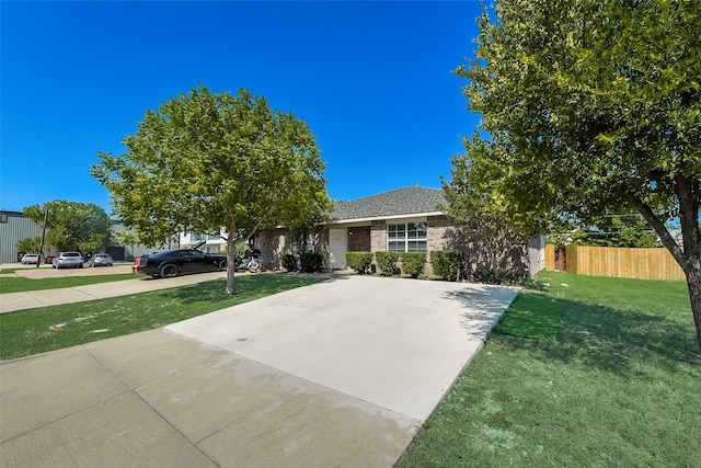 view of front of home with driveway, brick siding, a front yard, and fence