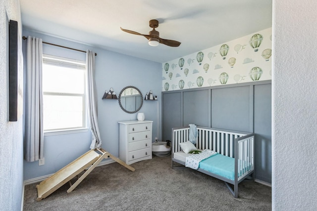 carpeted bedroom featuring wallpapered walls, a decorative wall, ceiling fan, and wainscoting