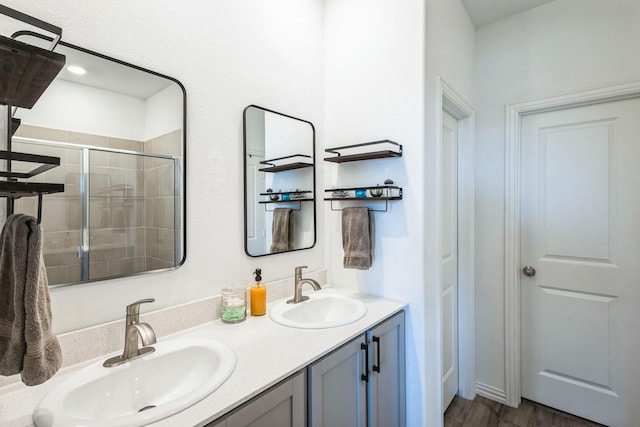 bathroom with double vanity, a stall shower, wood finished floors, and a sink