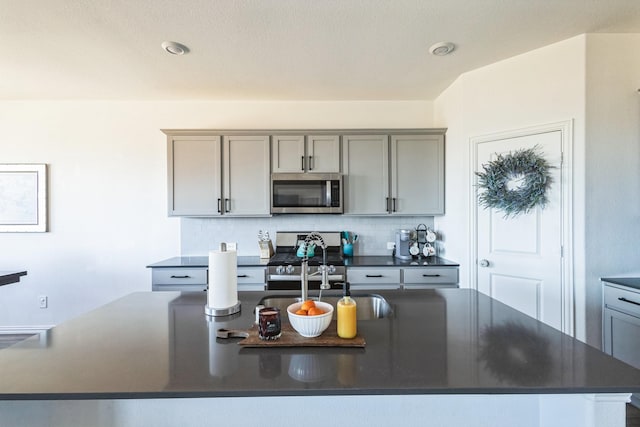 kitchen with dark countertops, gray cabinets, appliances with stainless steel finishes, and tasteful backsplash