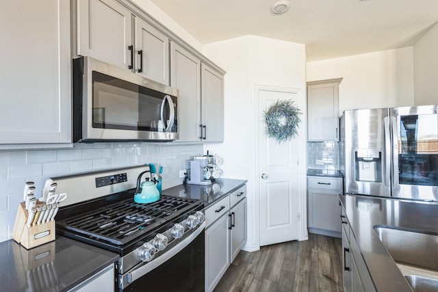 kitchen with dark countertops, gray cabinetry, decorative backsplash, stainless steel appliances, and dark wood-style flooring