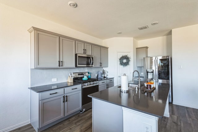 870 Sitwell Dr, Fate, TX 75087 - kitchen with stainless steel appliances, dark countertops, gray cabinetry, dark wood-style flooring, and decorative backsplash