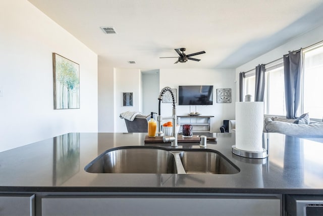 kitchen with visible vents, a ceiling fan, a sink, dark countertops, and open floor plan