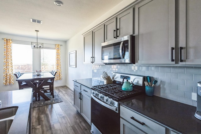 kitchen featuring gray cabinetry, stainless steel appliances, dark wood-type flooring, dark countertops, and tasteful backsplash