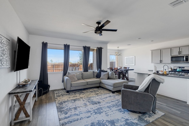 living room featuring visible vents, ceiling fan with notable chandelier, dark wood-type flooring, and baseboards