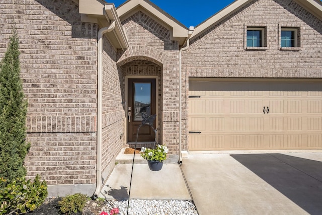 entrance to property featuring a garage, brick siding, and driveway