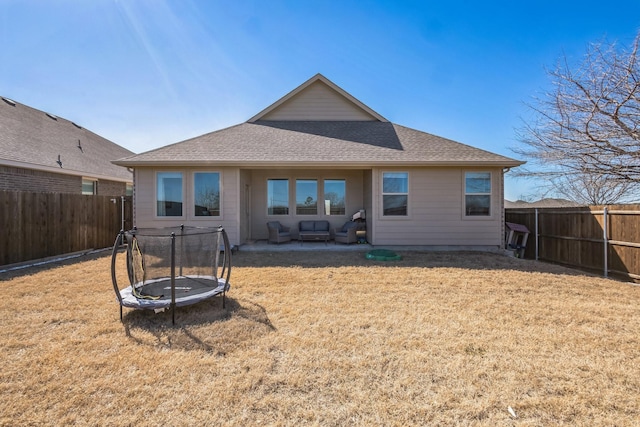 back of property featuring a shingled roof, a trampoline, a yard, a fenced backyard, and a patio area