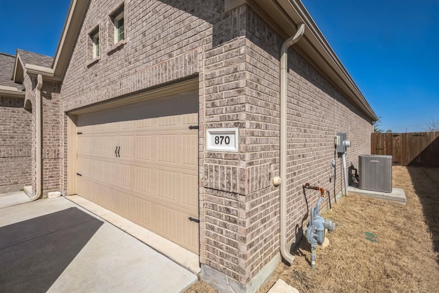 view of home's exterior with brick siding, fence, roof with shingles, central AC, and driveway