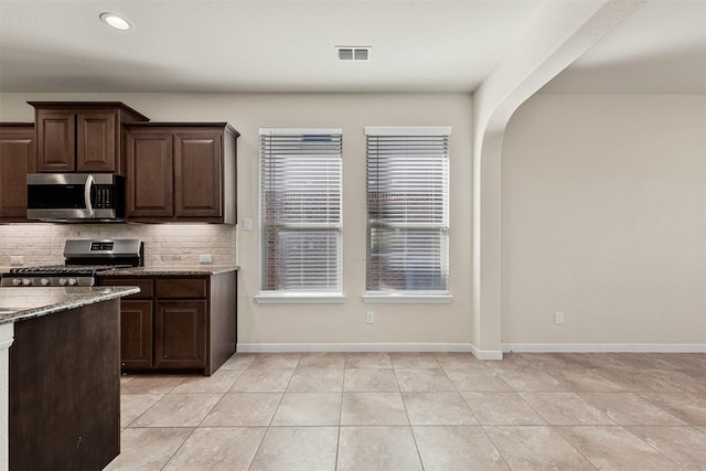 kitchen with light stone counters, backsplash, stainless steel appliances, dark brown cabinetry, and baseboards