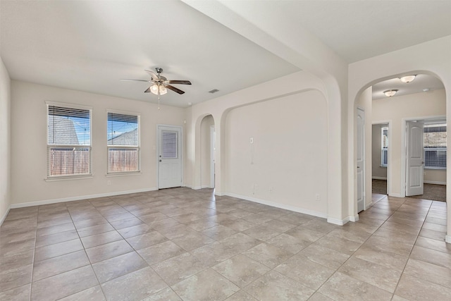 unfurnished room featuring arched walkways, light tile patterned floors, baseboards, and a ceiling fan