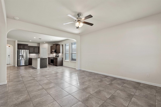 unfurnished living room with a sink, baseboards, arched walkways, and ceiling fan