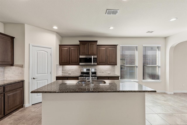 kitchen with stainless steel microwave, visible vents, dark stone counters, arched walkways, and a sink