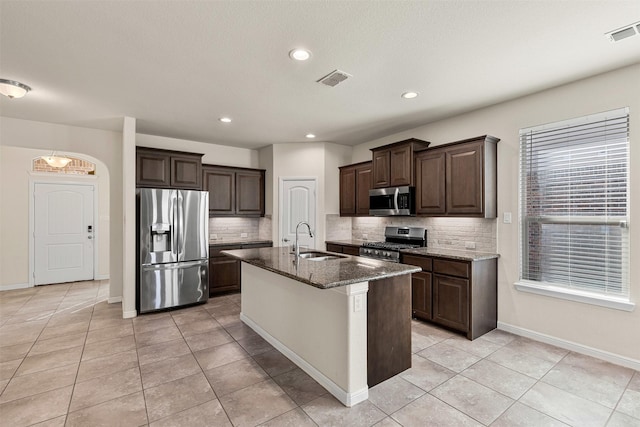 kitchen featuring visible vents, dark brown cabinets, dark stone countertops, stainless steel appliances, and a sink