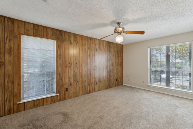 carpeted empty room with wooden walls, ceiling fan, and a textured ceiling