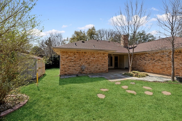 rear view of house with a shingled roof, a chimney, a lawn, a patio area, and brick siding