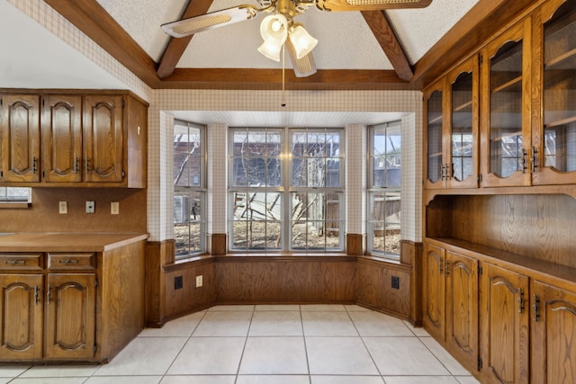 kitchen featuring a ceiling fan, vaulted ceiling with beams, brown cabinetry, and a textured ceiling