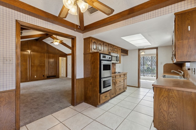 kitchen featuring wallpapered walls, light carpet, appliances with stainless steel finishes, a ceiling fan, and a sink