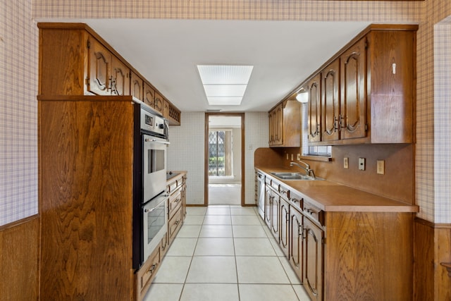 kitchen with a sink, wallpapered walls, double oven, light tile patterned flooring, and light countertops