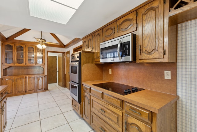 kitchen featuring lofted ceiling, light tile patterned floors, brown cabinetry, and appliances with stainless steel finishes