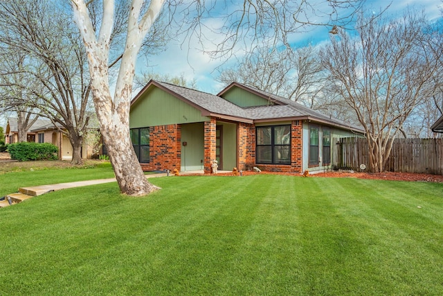 ranch-style house featuring brick siding, roof with shingles, a front yard, and fence