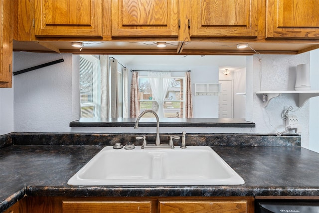 kitchen with open shelves, a sink, dark countertops, a textured wall, and brown cabinets