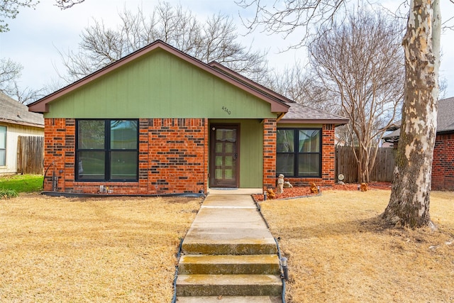 view of front of house featuring brick siding, a shingled roof, a front yard, and fence