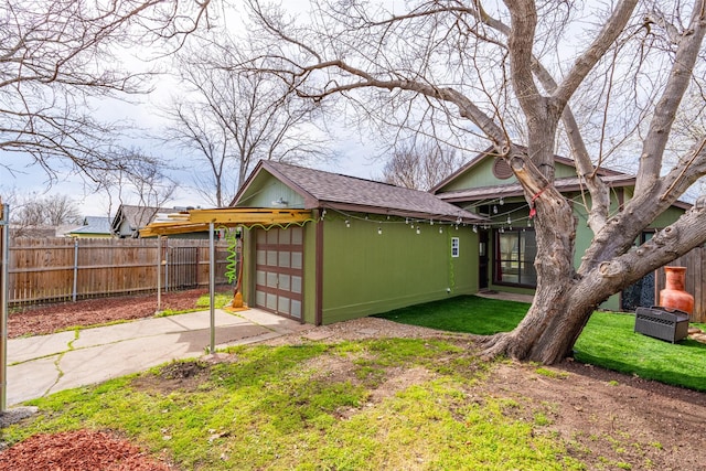 exterior space with a lawn, fence, roof with shingles, concrete driveway, and a garage