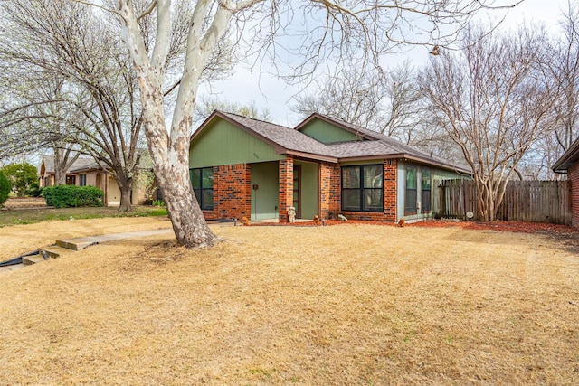 view of front of property featuring brick siding, a shingled roof, a front yard, and fence