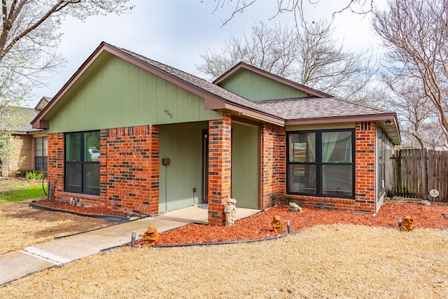 view of front of property with brick siding, a shingled roof, and fence