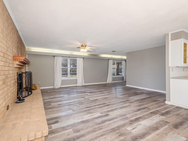 unfurnished living room with a fireplace, a textured ceiling, wood finished floors, and ceiling fan