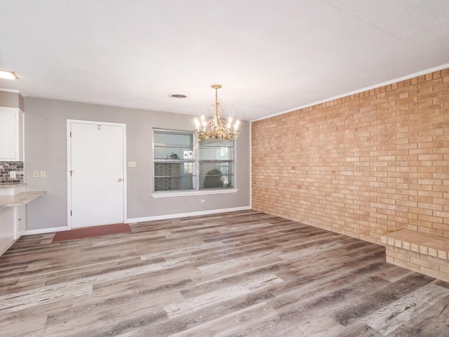 unfurnished dining area with wood finished floors, visible vents, baseboards, brick wall, and a notable chandelier