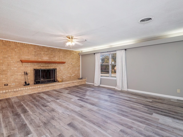 unfurnished living room with wood finished floors, visible vents, a fireplace, ceiling fan, and a textured ceiling