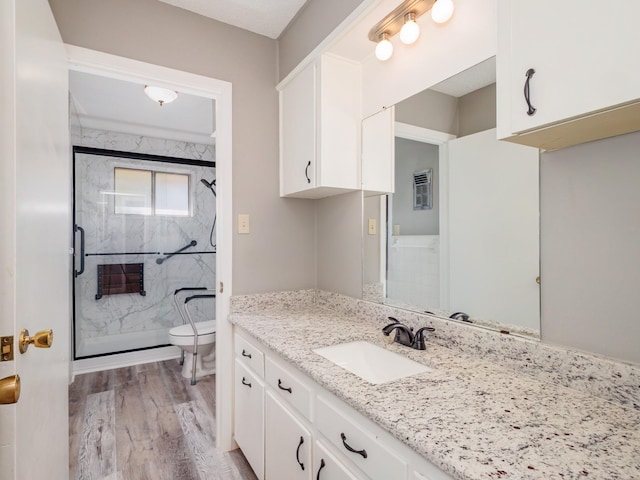 bathroom featuring a marble finish shower, toilet, vanity, and wood finished floors