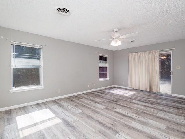 spare room featuring wood finished floors, baseboards, visible vents, ceiling fan, and a textured ceiling