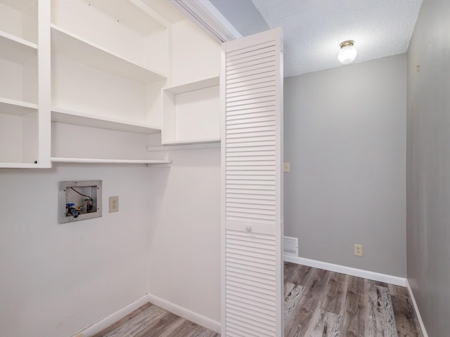 clothes washing area with baseboards, laundry area, hookup for a washing machine, wood finished floors, and a textured ceiling